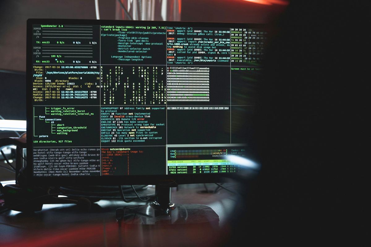 A monitor in a dim room showing several tiled terminal sessions with green system-monitoring output.