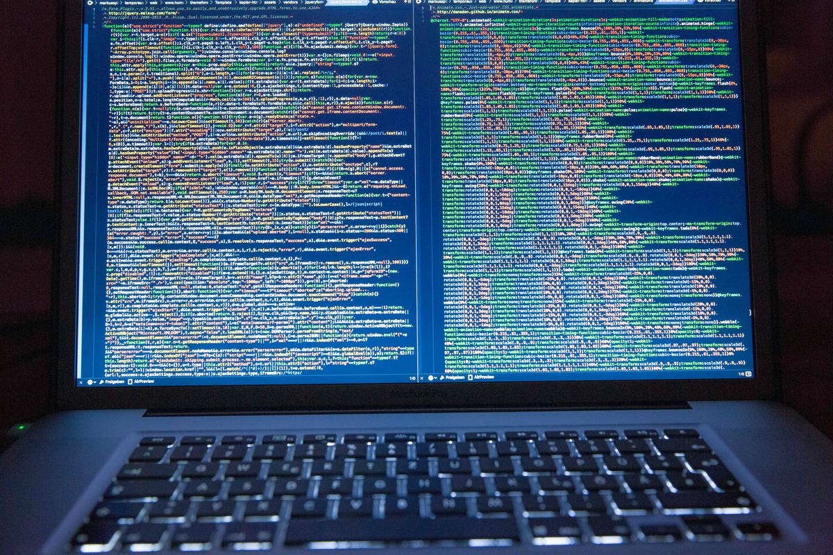 An open laptop in a dark room displaying two panes of syntax-highlighted source code.